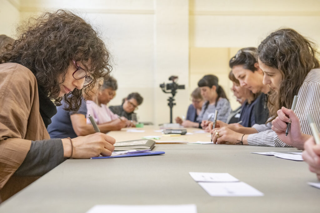 A group of people sitting at a long table writing.