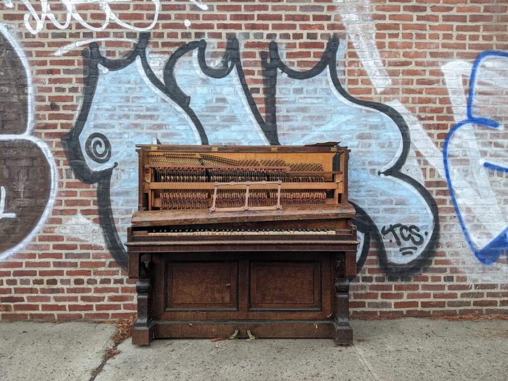 A dilapidated piano sitting outside on a brick wall covered in graffiti 